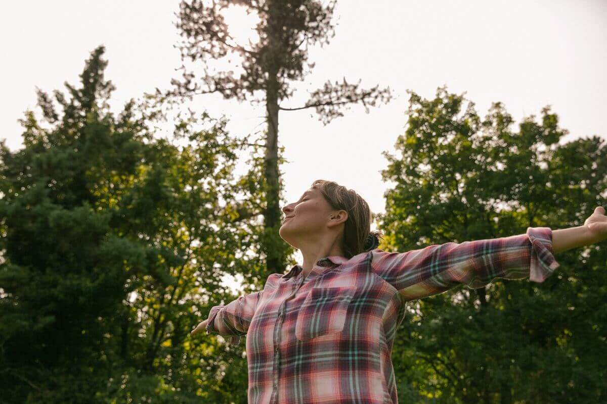 Eszter standing in a forest with open arms, breathing in.