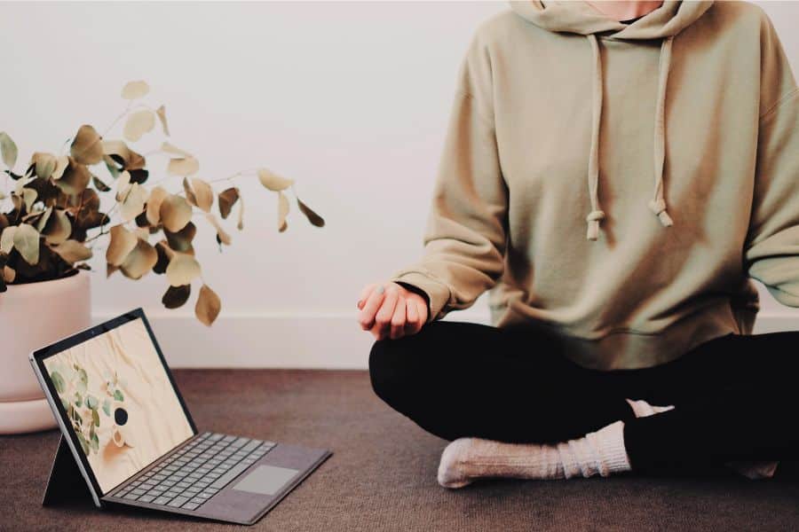 A person sitting on the floor in lotus pose with an open laptop next to them.