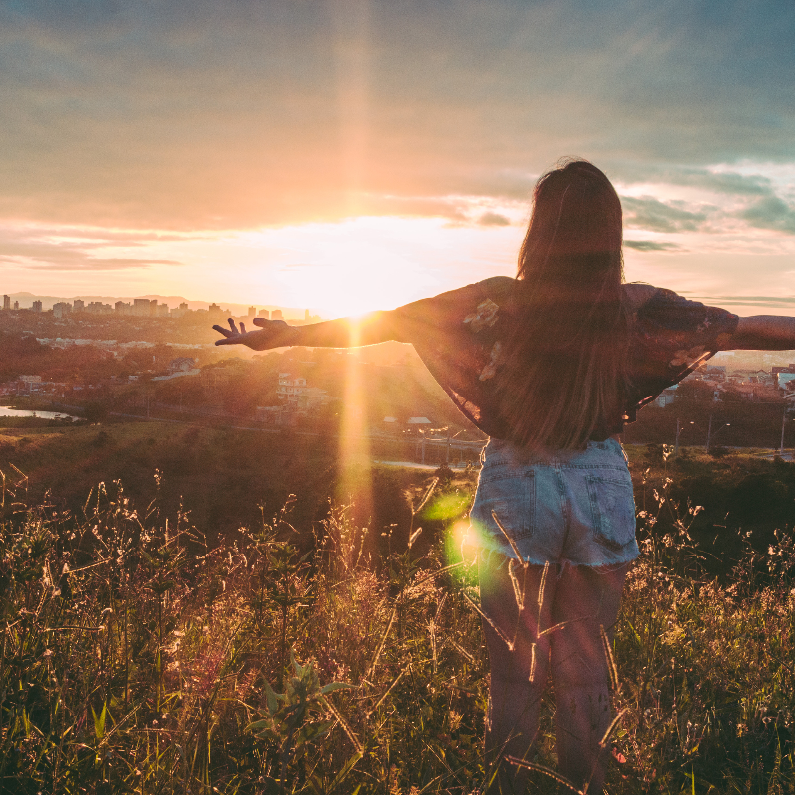 Woman standing in nature enjoying the sunset with arms wide open.